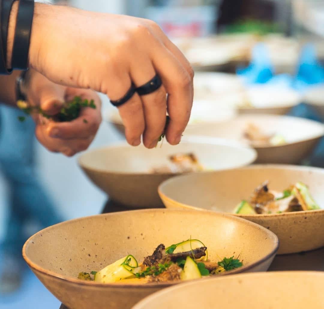 Chef garnishing ceramic bowls with fresh herbs at a private event