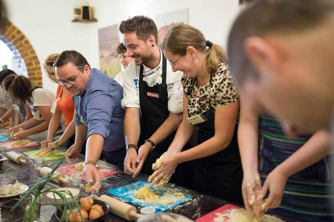 Adults laughing and kneading dough together in a hands-on cooking workshop