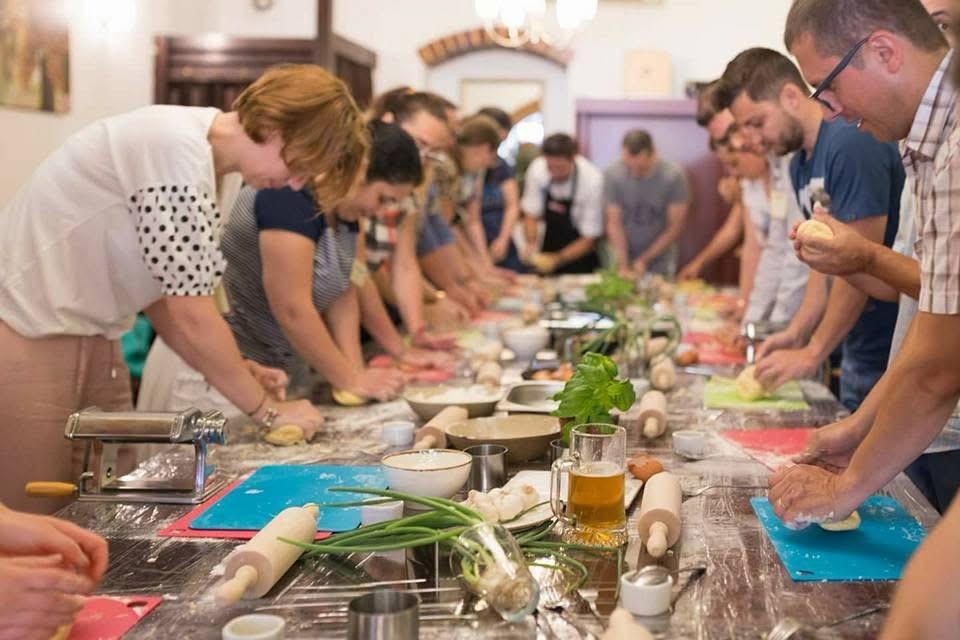 Long communal table of guests rolling dough at a rumen. workshop